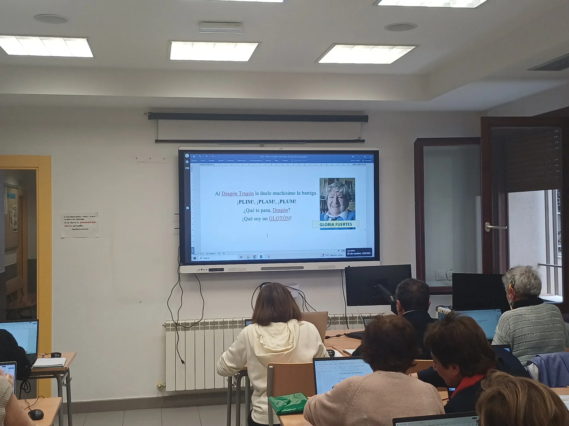 Pantalla del aula con un texto de Gloria Fuertes en Microsoft Word y alumnado practicando con sus ordenadores.